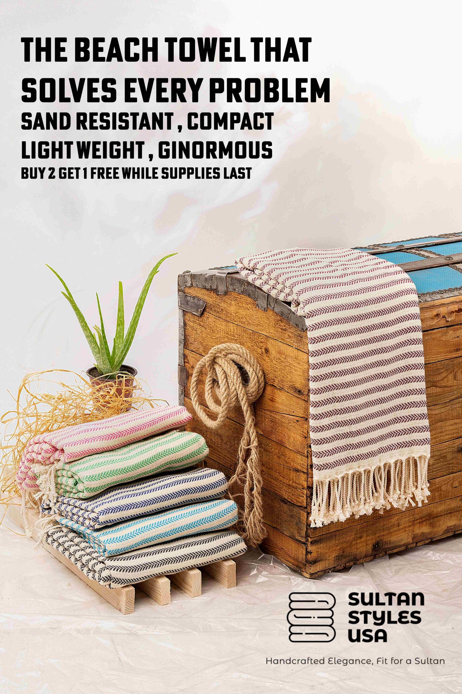 Stack of beach towels with a wooden chest on sand, Sultan Styles USA branding visible.